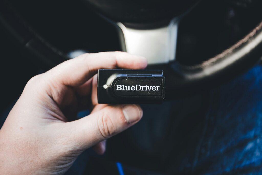 Services Close-up of a hand holding a BlueDriver wireless diagnostic tool inside a vehicle.